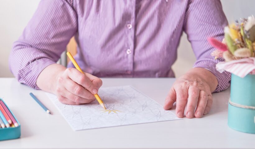 Elderly woman's hand painting an abstract pattern from adult coloring pages.