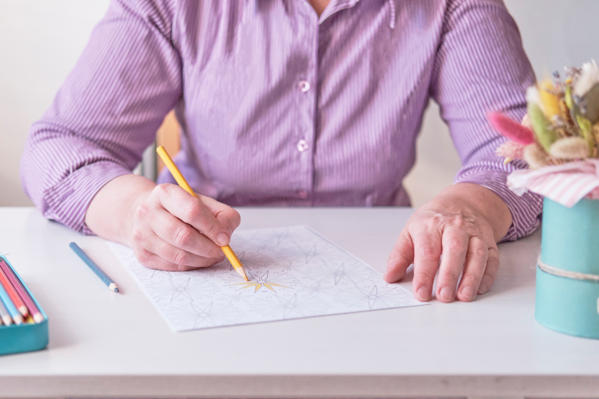 Elderly woman's hand painting an abstract pattern from adult coloring pages.