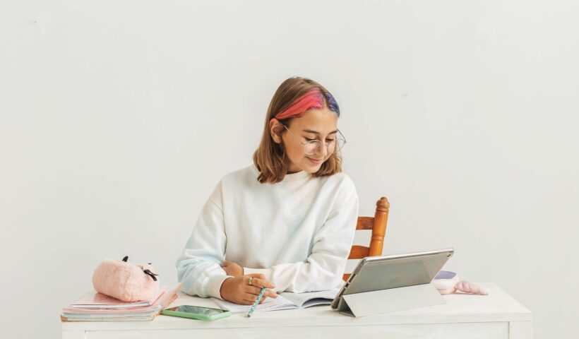 Little teenage girl with multi-colored hair learns online using a laptop.