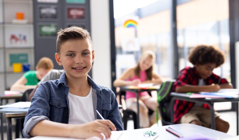 Portrait of smiling caucasian schoolboy working at his desk in class, with copy space