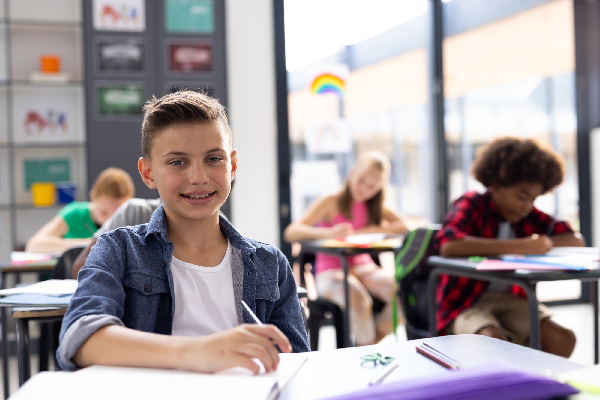 Portrait of smiling caucasian schoolboy working at his desk in class, with copy space