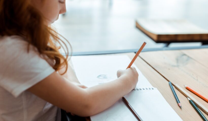 selective focus of redhead kid drawing on paper with color pencil