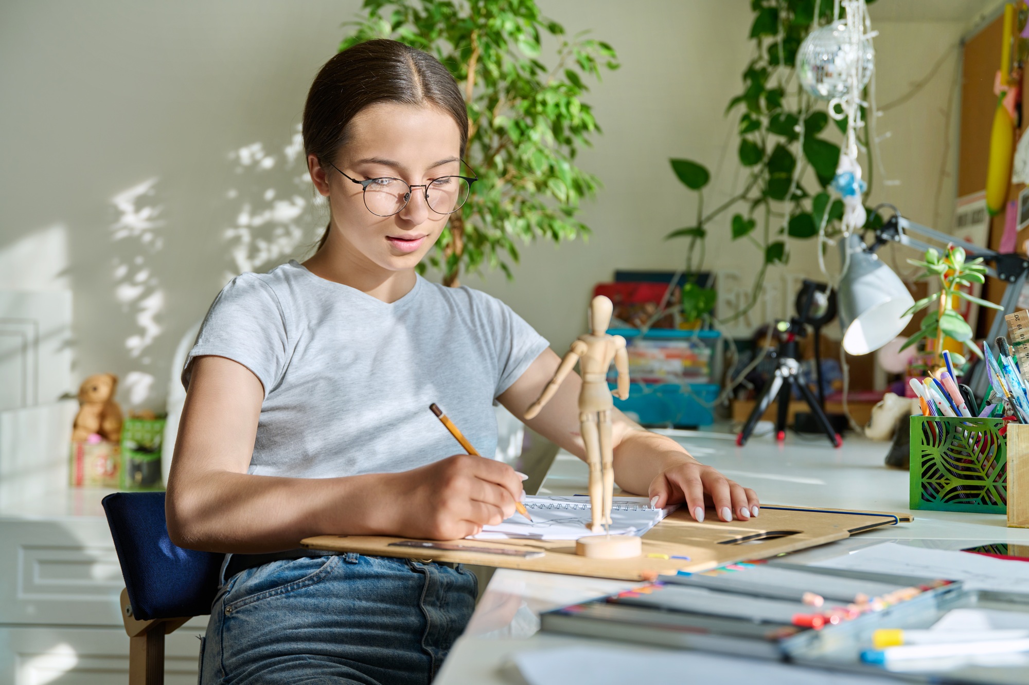 Teenage creative girl artist drawing with a pencil, sitting at the table at home
