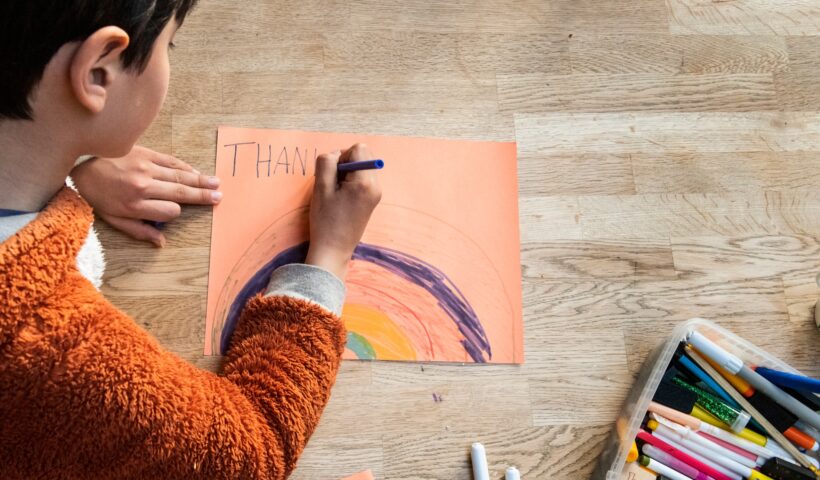 Young child focused on drawing a colorful rainbow on paper.