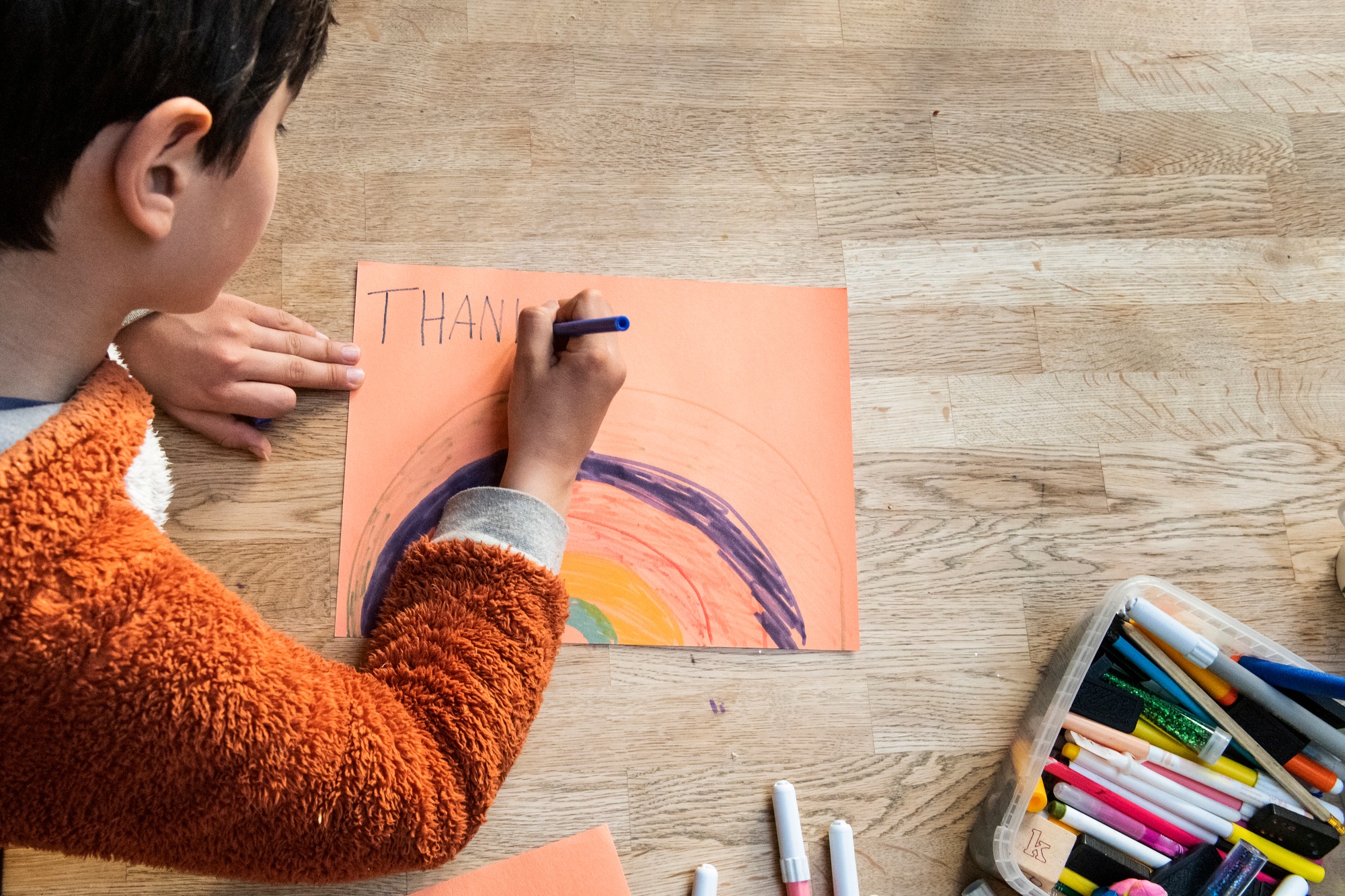 Young child focused on drawing a colorful rainbow on paper.