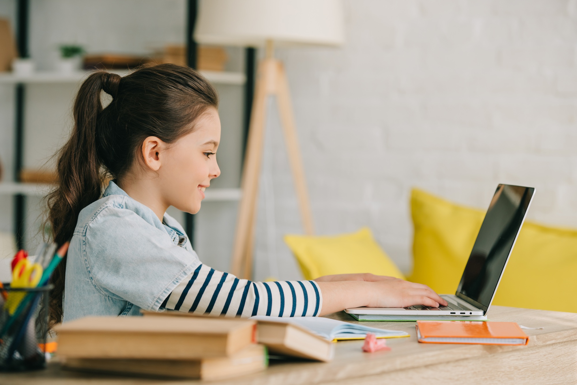 side view of adorable child using laptop while sitting at desk with books and doing homework