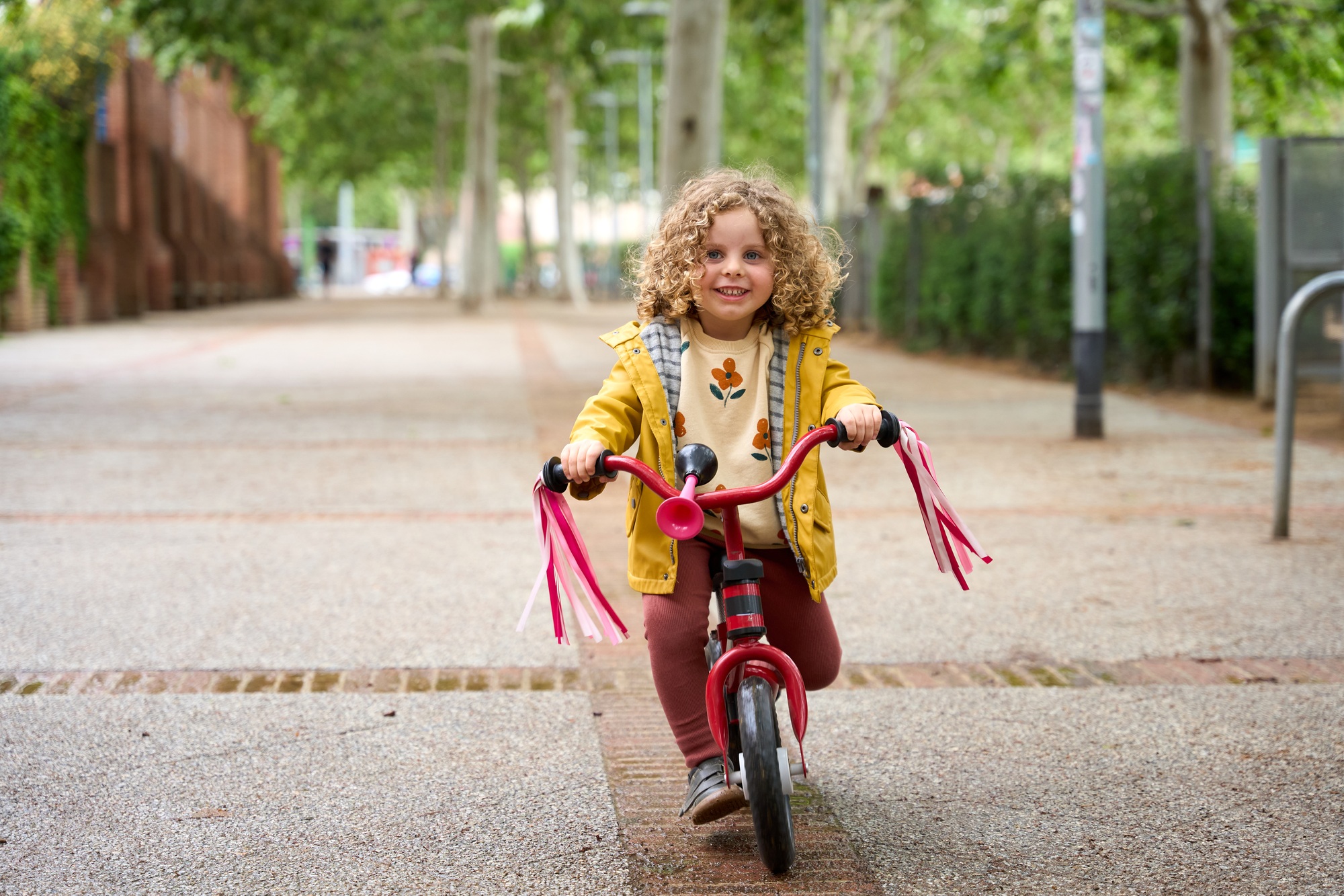 A young girl is riding a red bike down a sidewalk