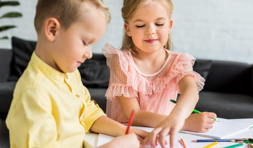 adorable siblings drawing with colored pencils at home