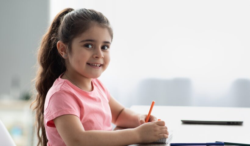 Beautiful Little Girl Siting At Table And Drawing With Colorful Pencils
