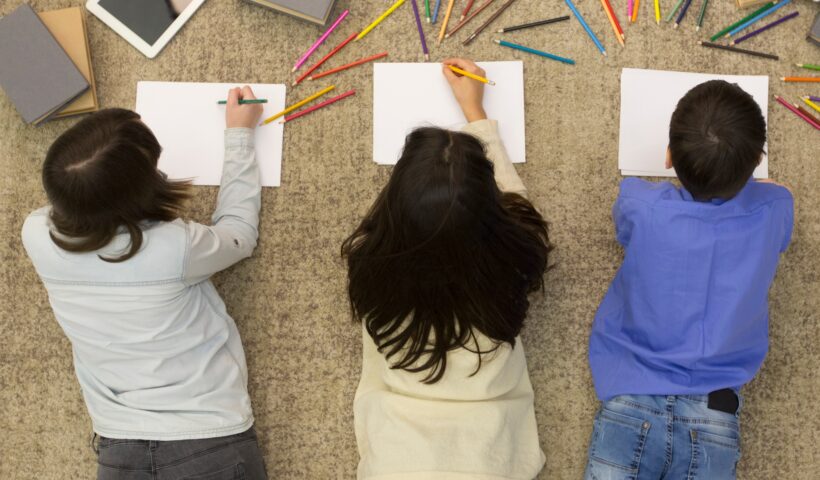 School children drawing with colored pencils on carpet