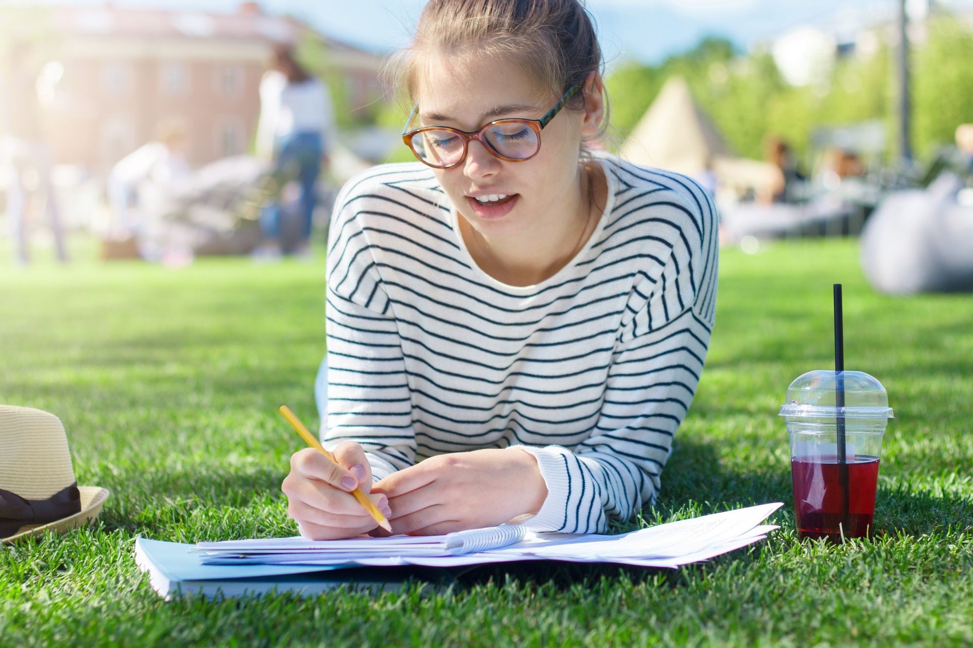 Student girl lying on green grass with notebook open in front, texting messages