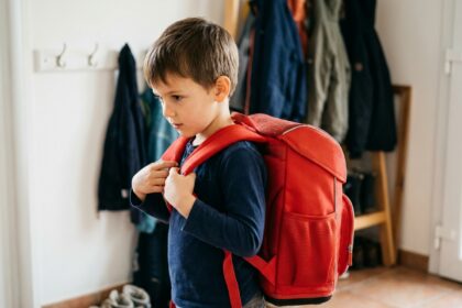 Jeune garçon essayant un cartable ergonomique rouge dans l'entrée de sa maison avant la rentrée scolaire
